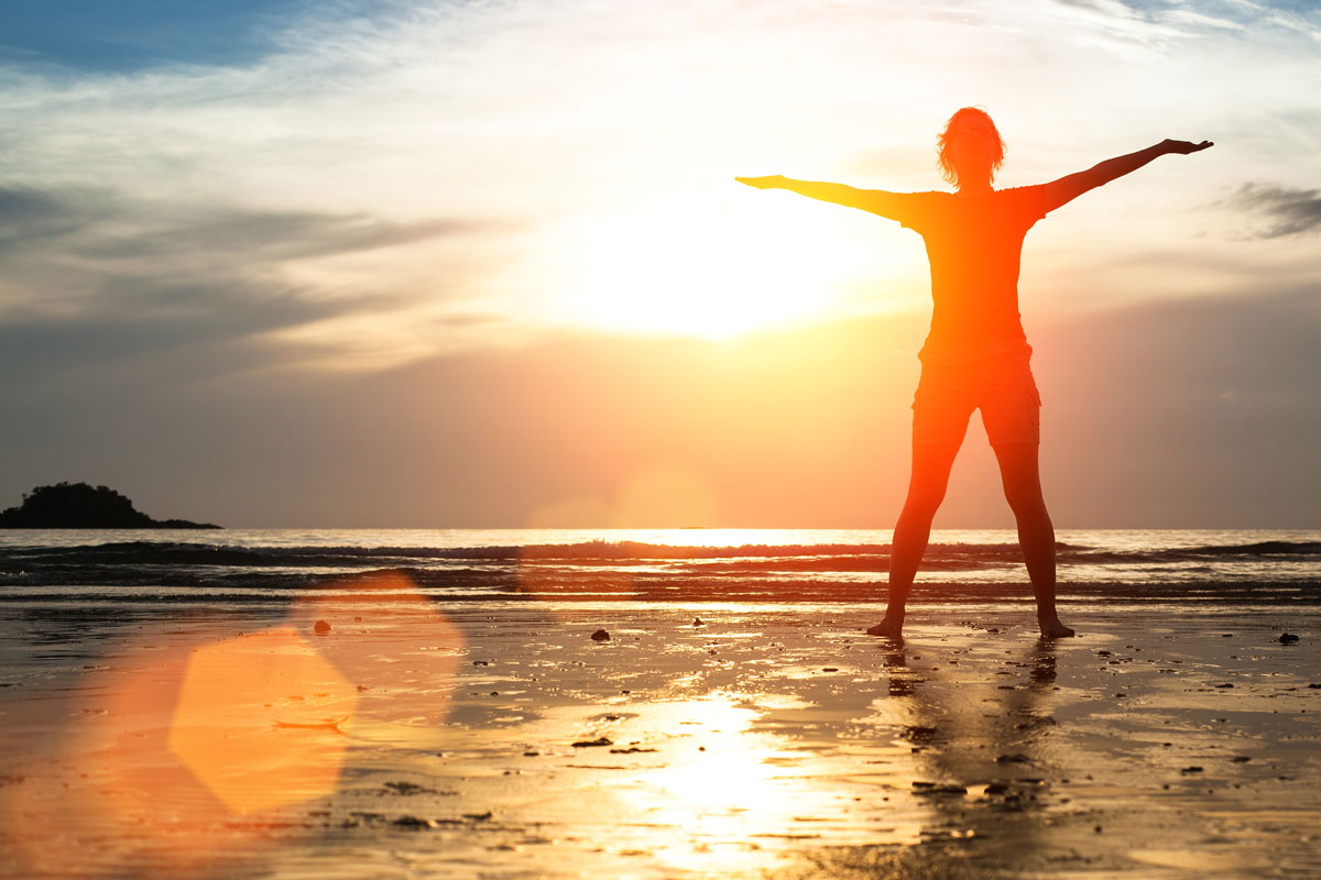 a silhouette of a person standing in prone position on the beach during sunrise