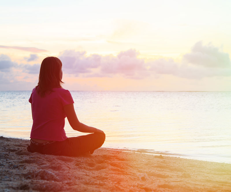 a lady on the beach sitting crossed legged during dusk