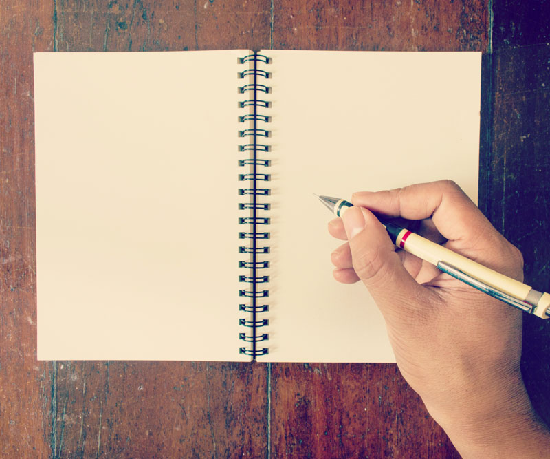 close up of a hand and pen above an empty notebook