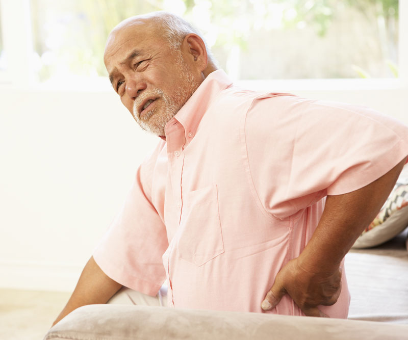 an older man sitting in a chair touching his lower back