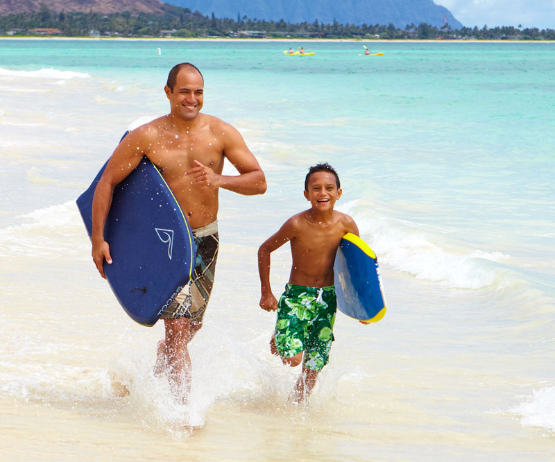 father and son with boogie boards running on the beach