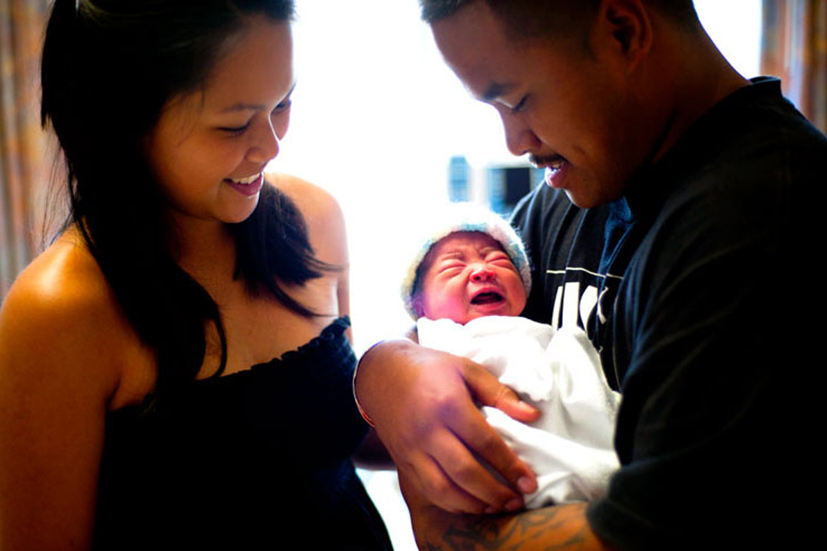 newborn baby in the arms of dad with mom smiling