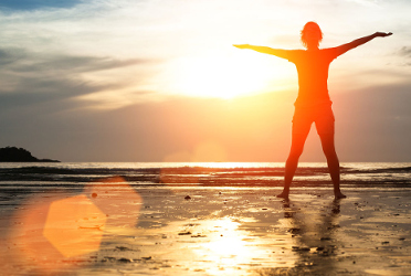 Silhouette of a person standing with arms outstretched on the beach during sunrise.