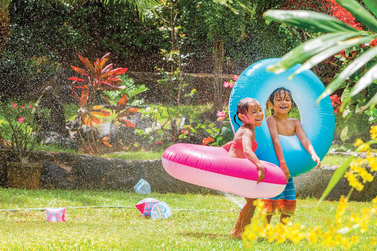 two kids playing in the yard with a sprinkler and blow up pool toys