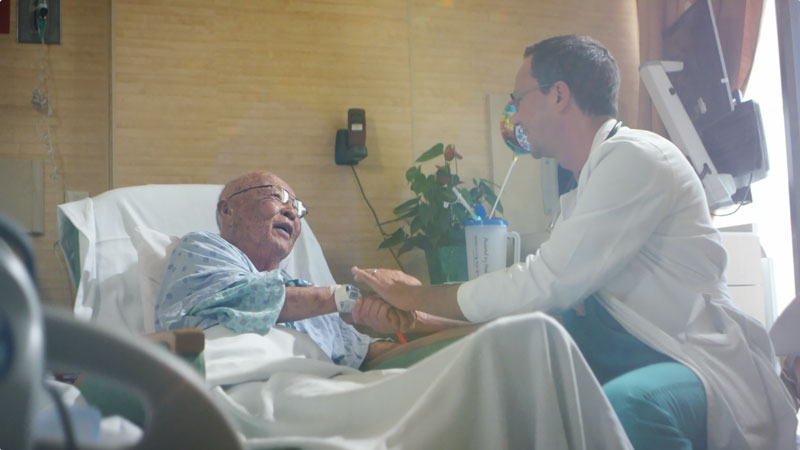 a patient in a bed shaking hands with a doctor
