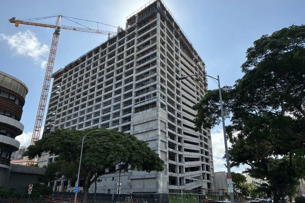 Street-level view of the parking building and tower crane under a blue sky.