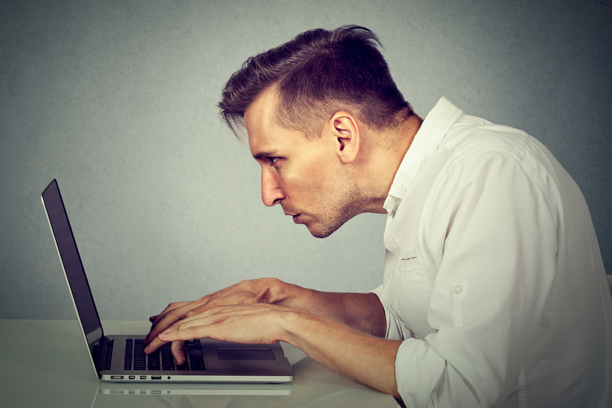 man crouched uncomfortably in front of his laptop