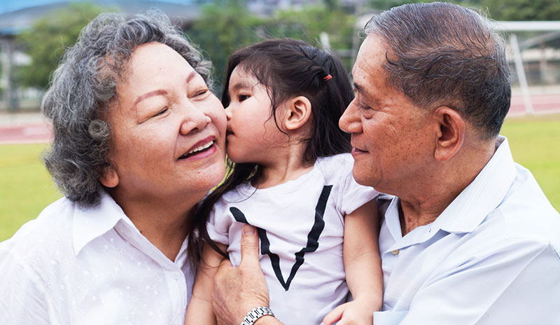 Photo of a little girl held by her grandfather kissing her grandmother