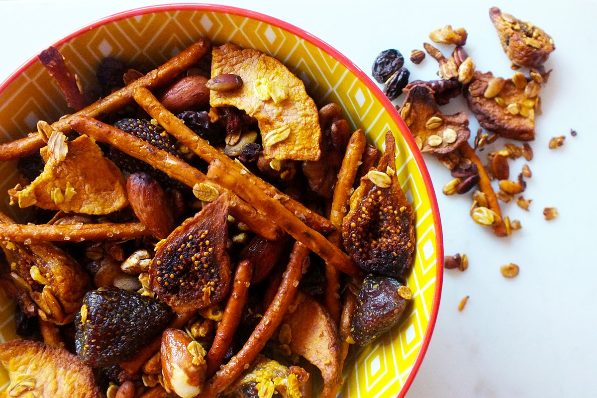 A yellow bowl sits on a marble counter top filled to the brim with Sweet & Salty Crunch Mix, with some extra mix overflowing onto the table top