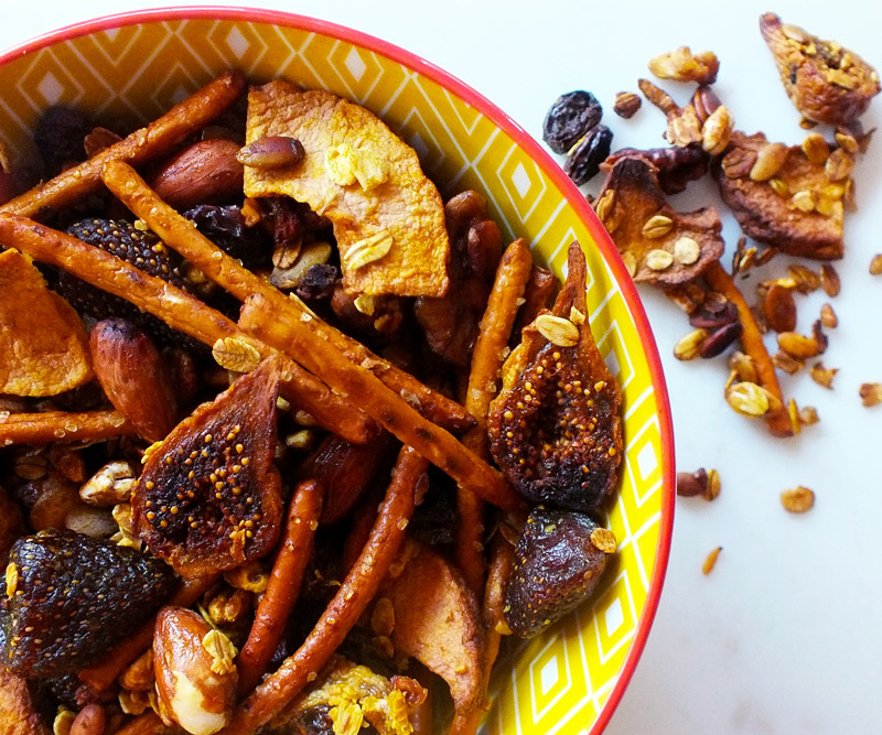 A yellow bowl sits on a marble counter top filled to the brim with Sweet & Salty Crunch Mix, with some extra mix overflowing onto the table top