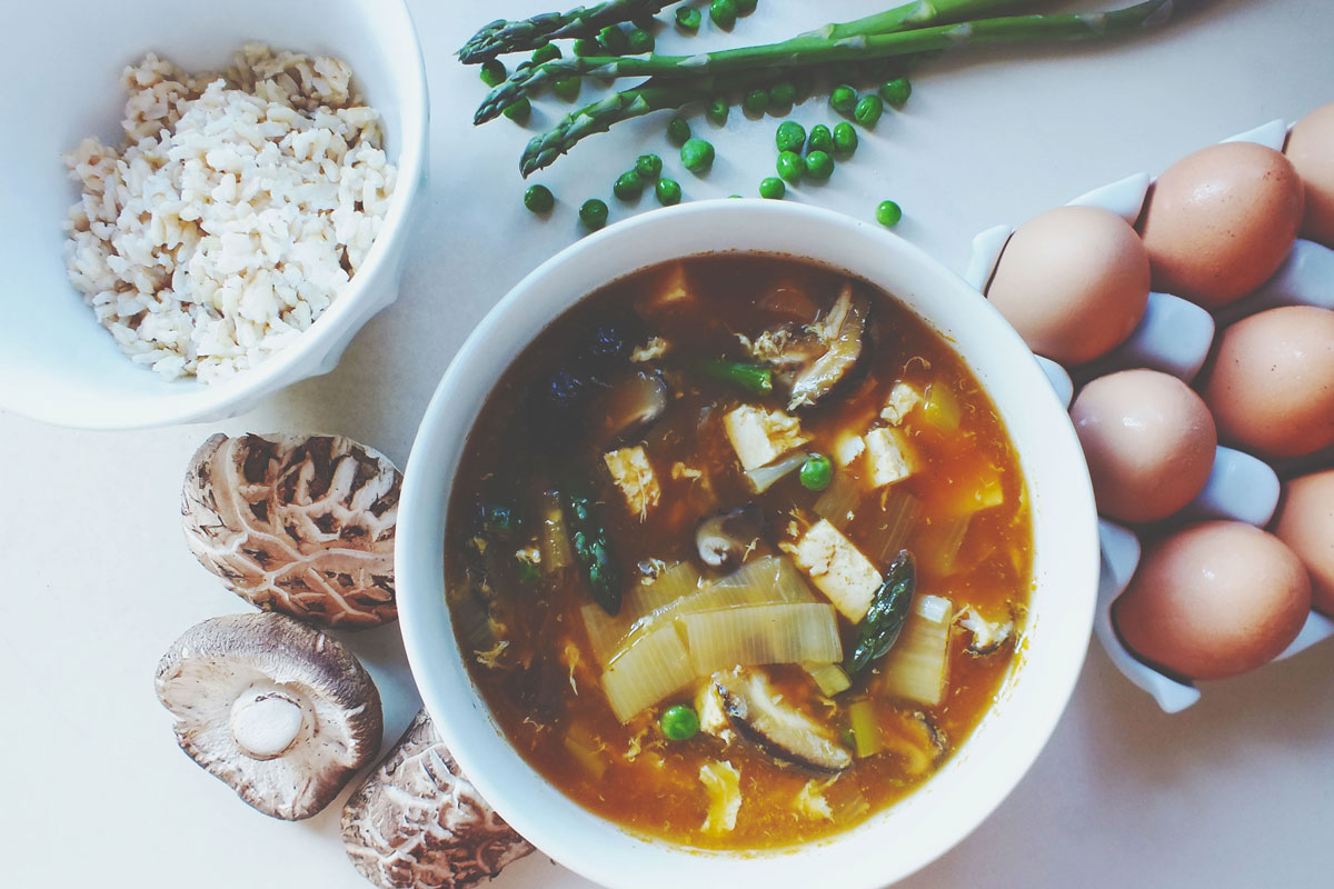 Springtime Egg Flower Soup in bowl surrounded by ingredients like mushrooms, eggs, rice, asparagus and peas