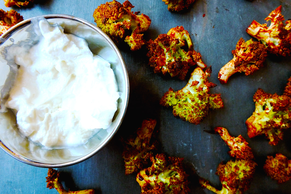 Spicy Buffalo Romanesco Bites scattered on a slate counter top next to a bowl of Greek yogurt dipping sauce