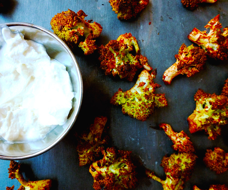 Spicy Buffalo Romanesco Bites scattered on a slate counter top next to a bowl of Greek yogurt dipping sauce