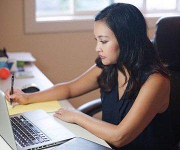 Women in front of computer writing on notepad