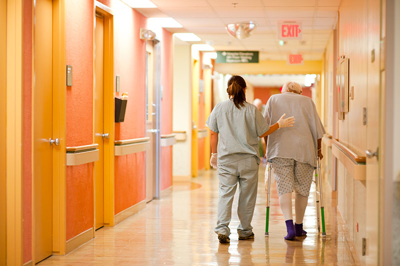 A patient and a health professional walking down a hallway inside a hospital.