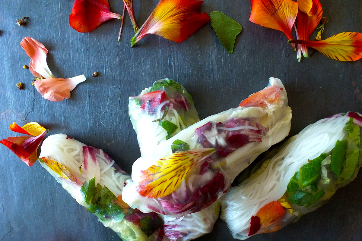 Garden of Eden Spring Rolls on a slate counter surrounded by orange and pink flowers