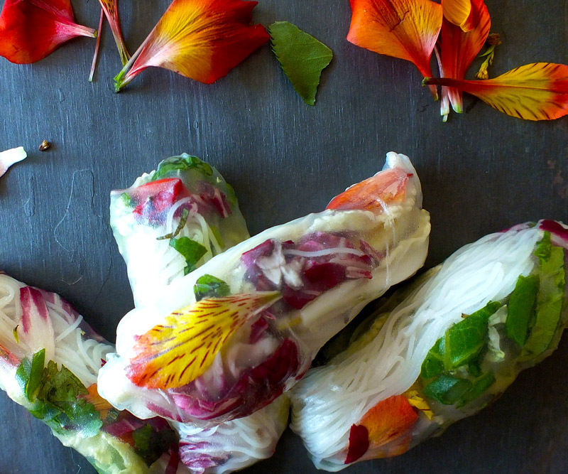 Garden of Eden Spring Rolls on a slate counter surrounded by orange and pink flowers