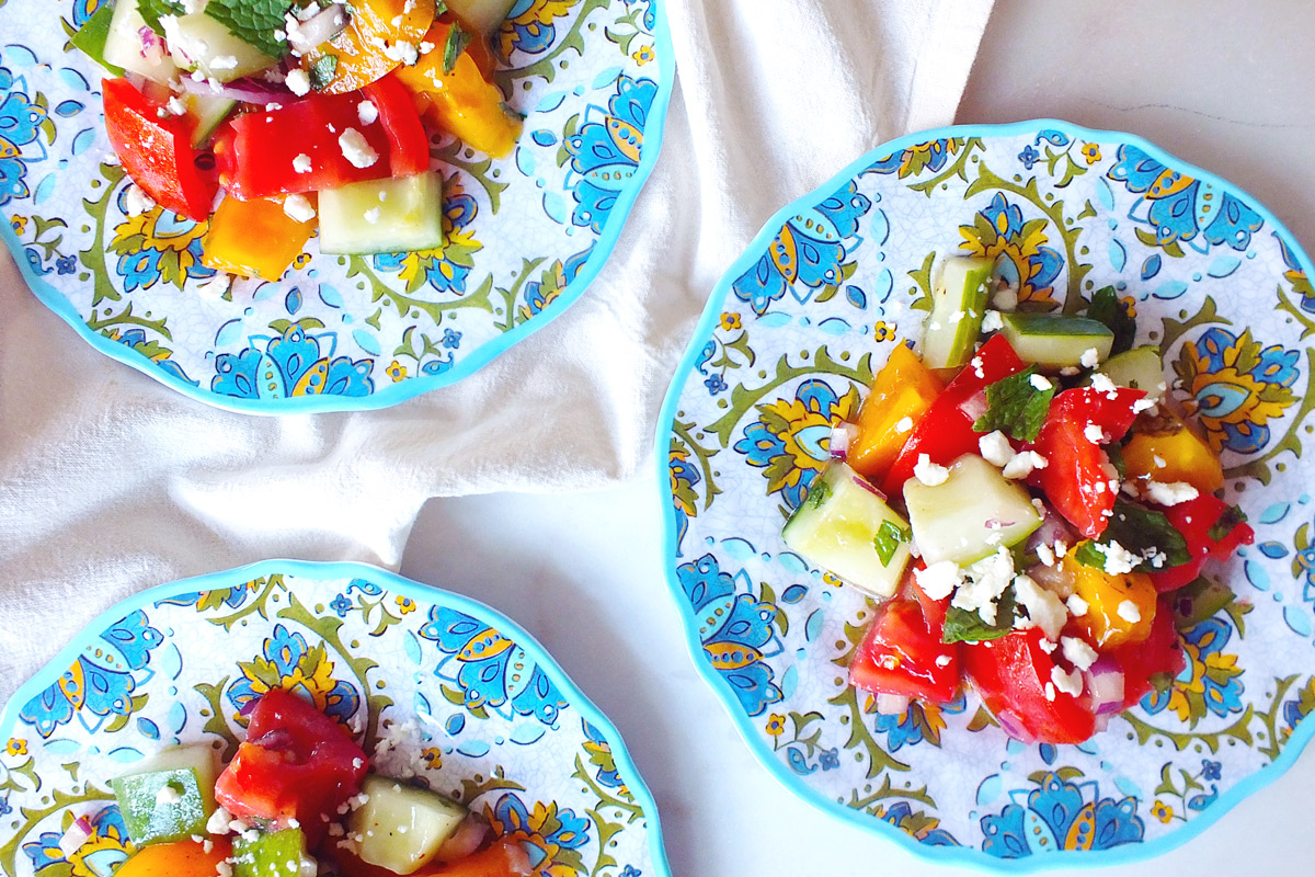 Three colorful plates of Tomato, Cucumber & Feta Summer Salad on a marble counter top and white dish towel