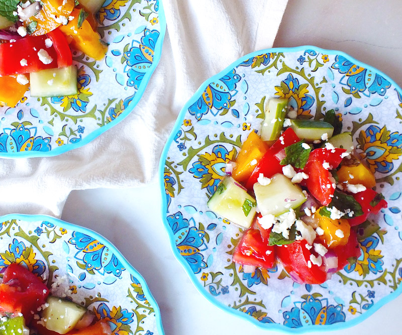 Three colorful plates of Tomato, Cucumber & Feta Summer Salad on a marble counter top and white dish towel