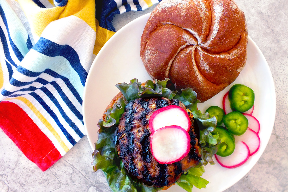 An open-faced Korean Barbecue Burger sitting on a white plate with a brightly colored, stripped towel next to it