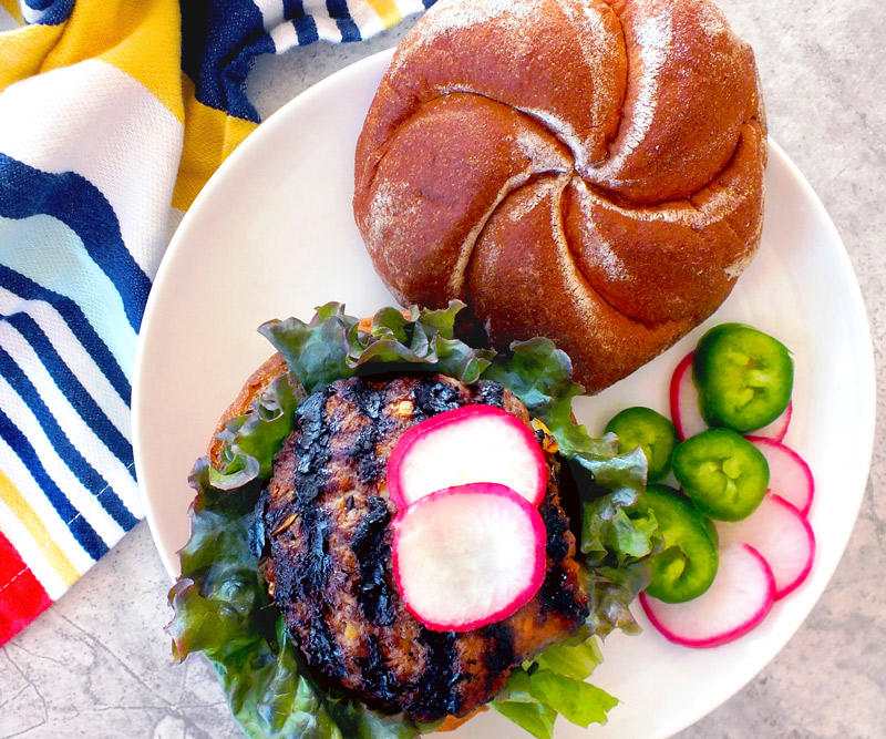 An open-faced Korean Barbecue Burger sitting on a white plate with a brightly colored, stripped towel next to it