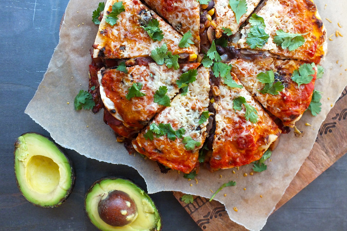 A freshly made Tex-Mex Tortilla Pie is presented on a wooden cutting board with an avocado, cut in half, next to it