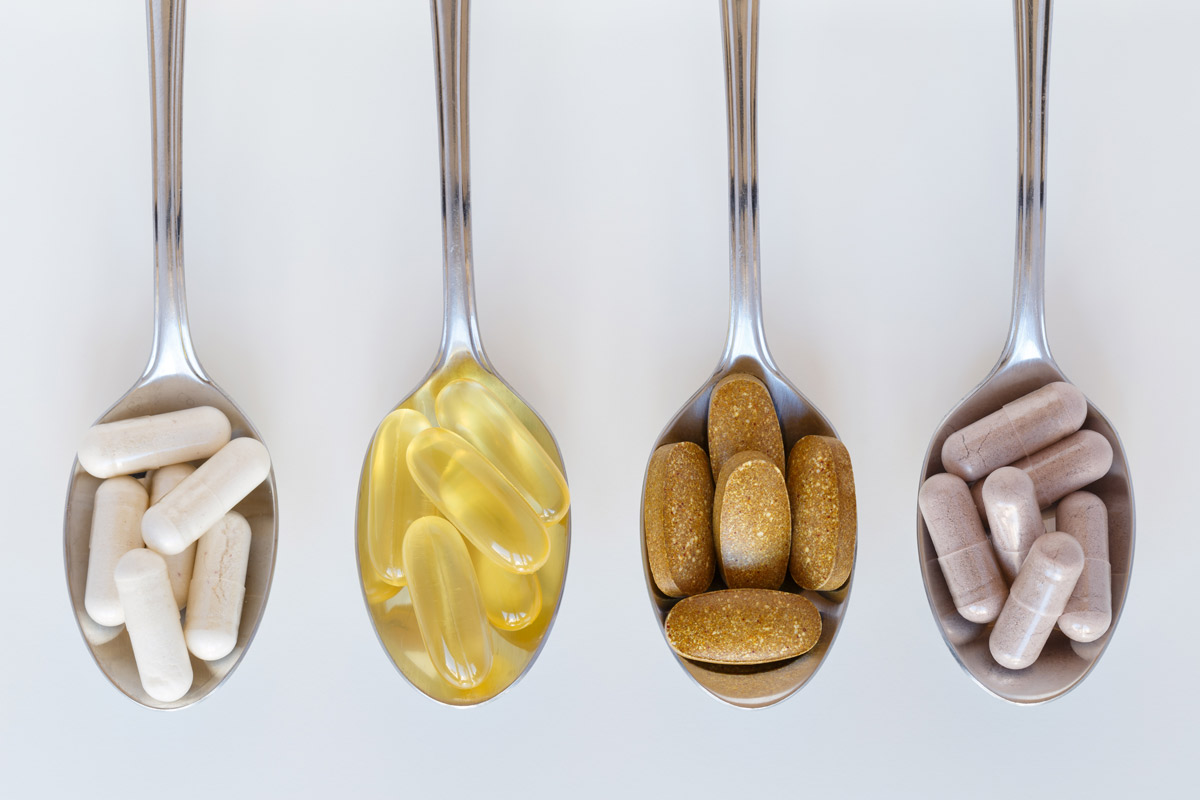 four spoons containing different vitamin and supplements pills set up in a line on a counter