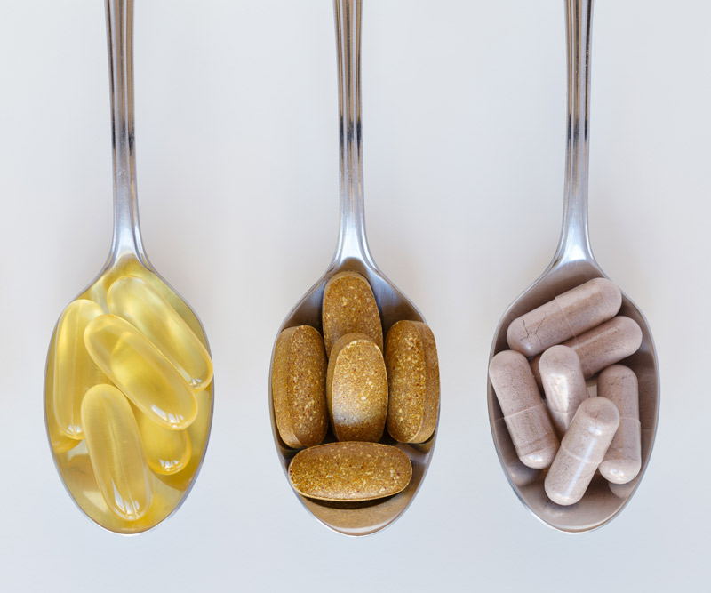 four spoons containing different vitamin and supplements pills set up in a line on a counter