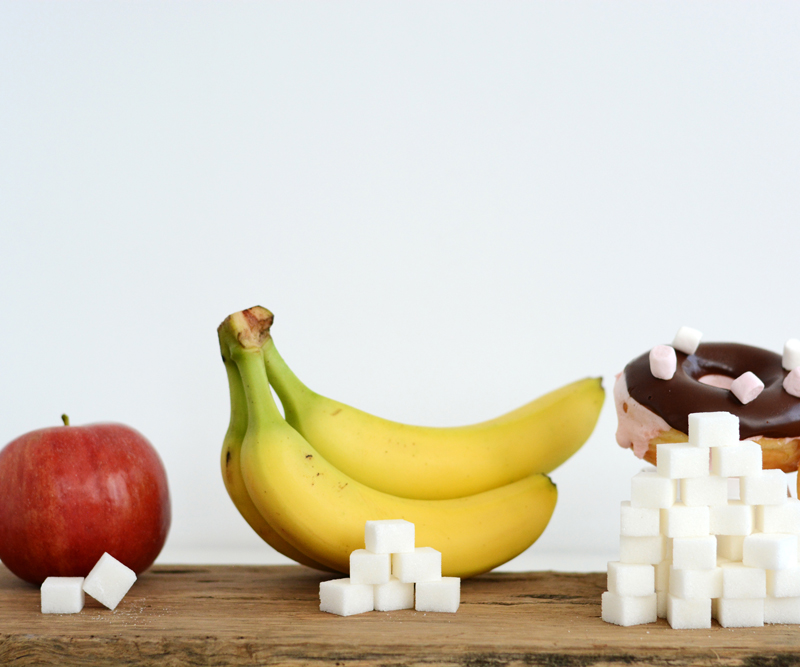 A photo shows an apple, banana and donuts with sugar cubes to depict how much sugar is found in each food item.