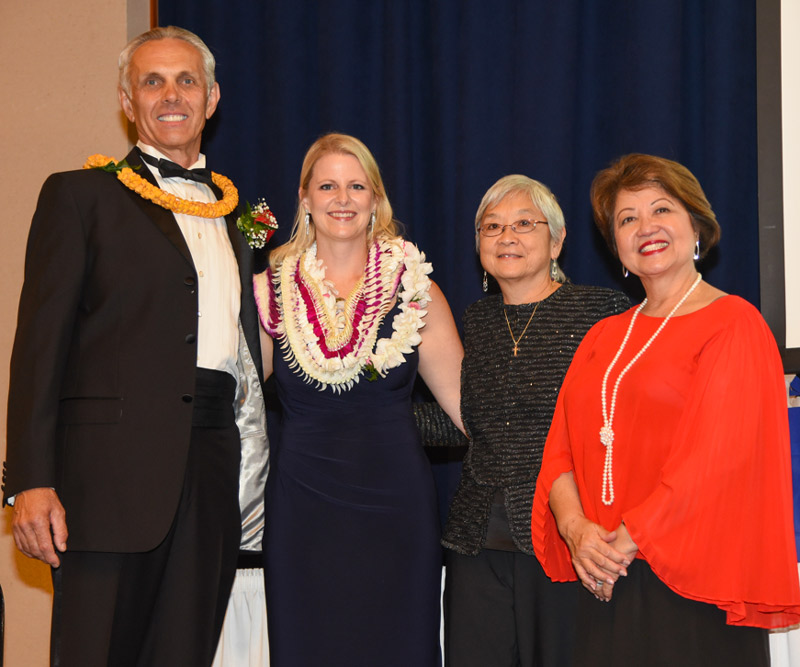 A man and three women stand on stage during a ceremony.