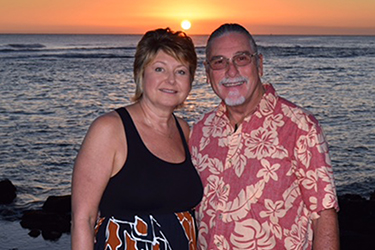 Women and man standing arm in arm at the beach smiling into camera