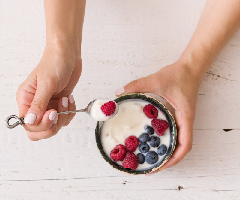 Woman's hands holding a spoon in one hand and a bowl of yogurt and fruit in the other