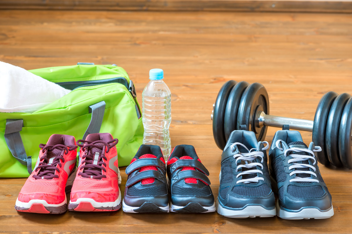 A pair of woman's, child's and man's running shoes sit in front of a gym bag, water bottle and weights to represent a family getting into shape together.