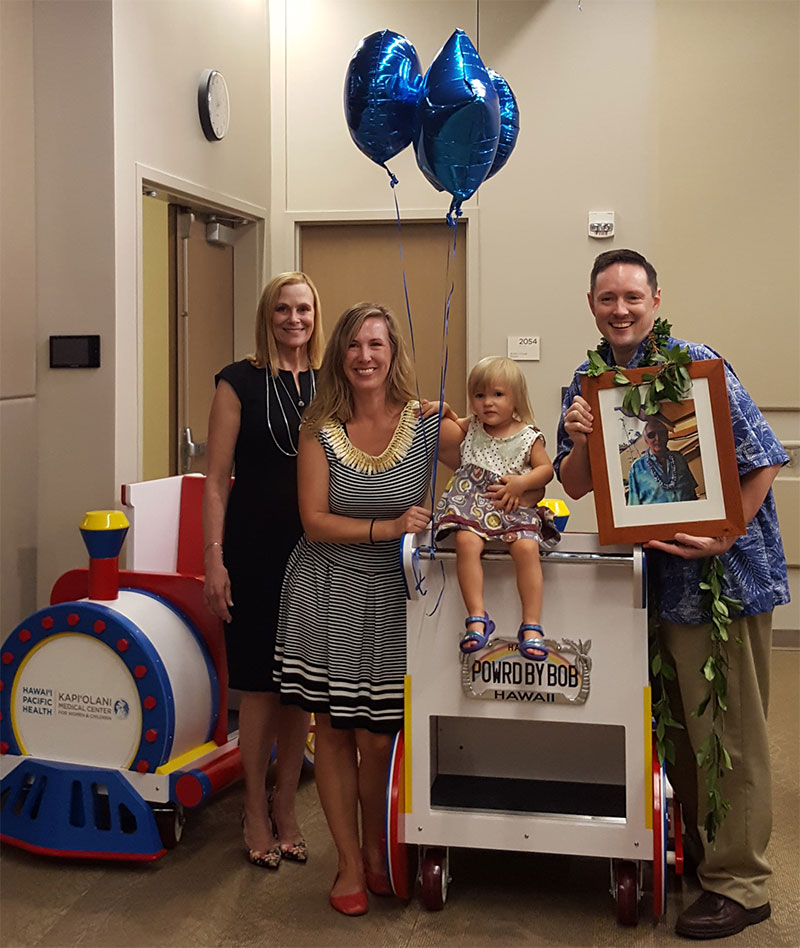 Two women, child and man standing next to two wooden trains