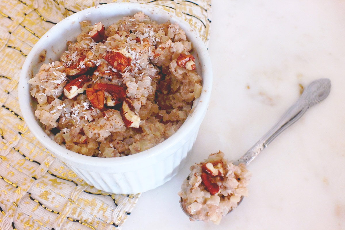 Bowl of Coconut Cauliflower "Rice" Pudding with a spoonful of pudding sitting next to the bowl