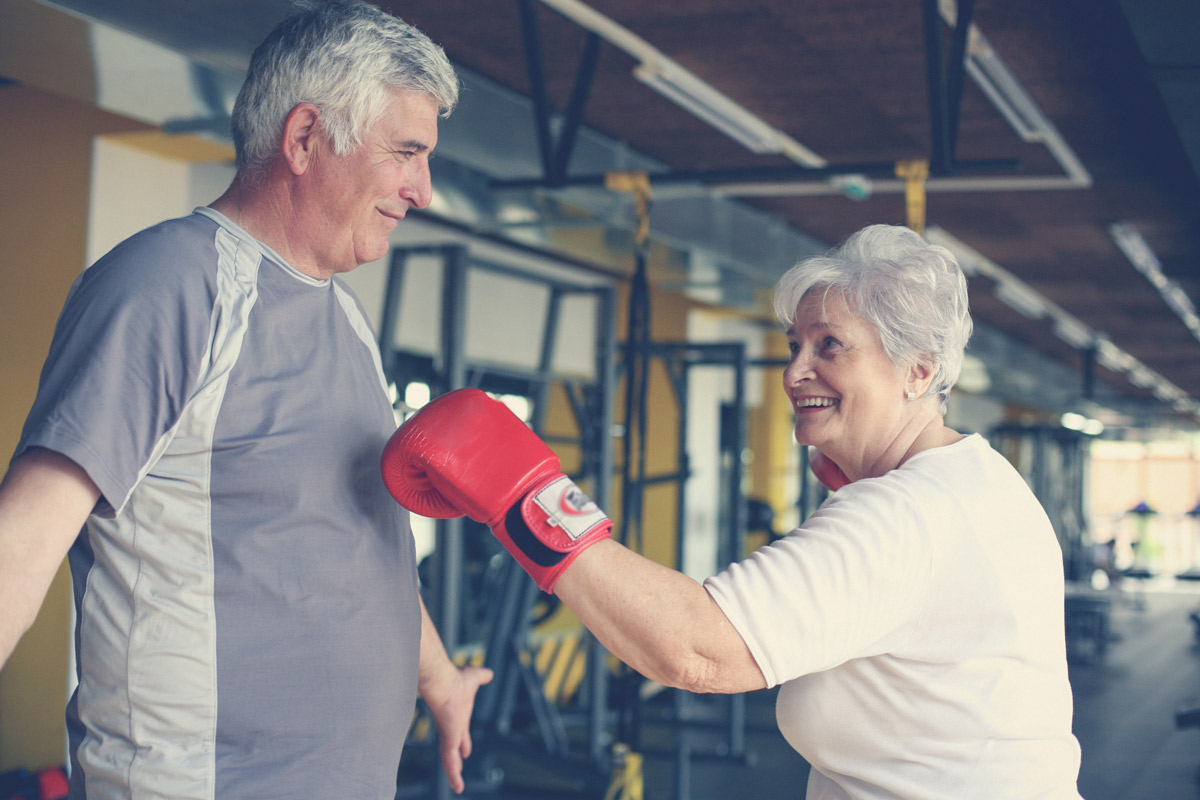 An older women playfully spars with her husband in a gym