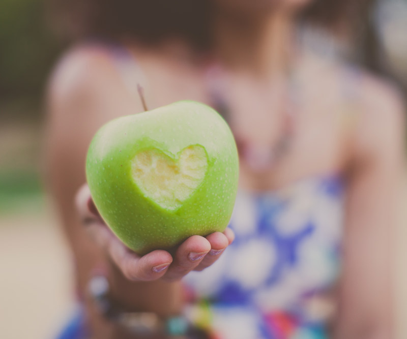 Woman holding an apple with a heart-shaped bite taken out of it