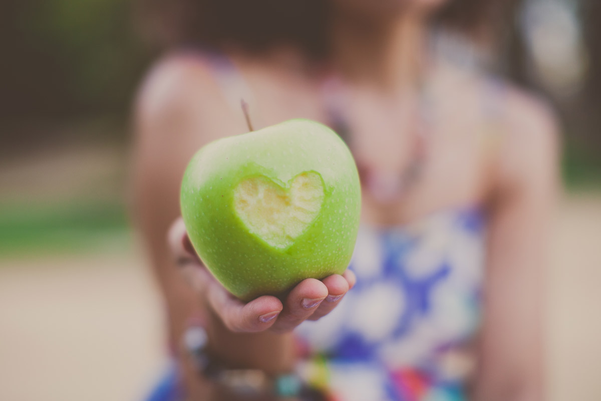 Woman holding an apple with a heart-shaped bite taken out of it