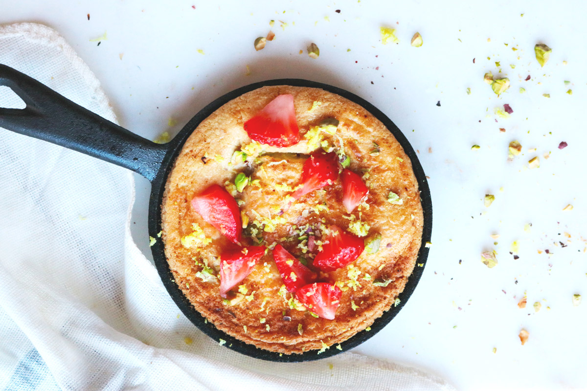 A Mini Dutch Baby baked in a cast iron skillet topped with strawberries and pistachios
