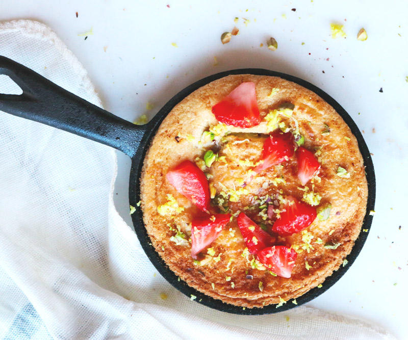 A Mini Dutch Baby baked in a cast iron skillet topped with strawberries and pistachios
