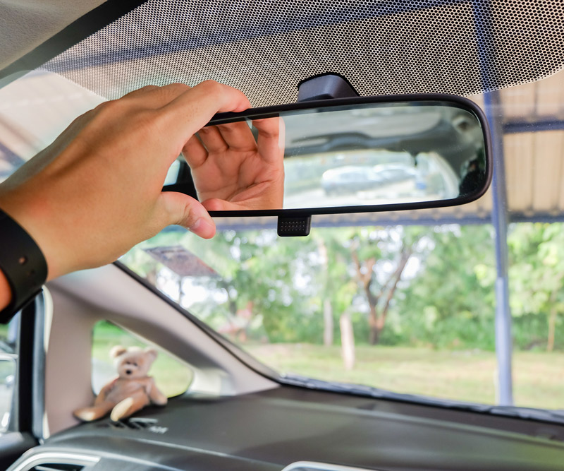 A man adjusts his review mirror of his car to better see out the back window