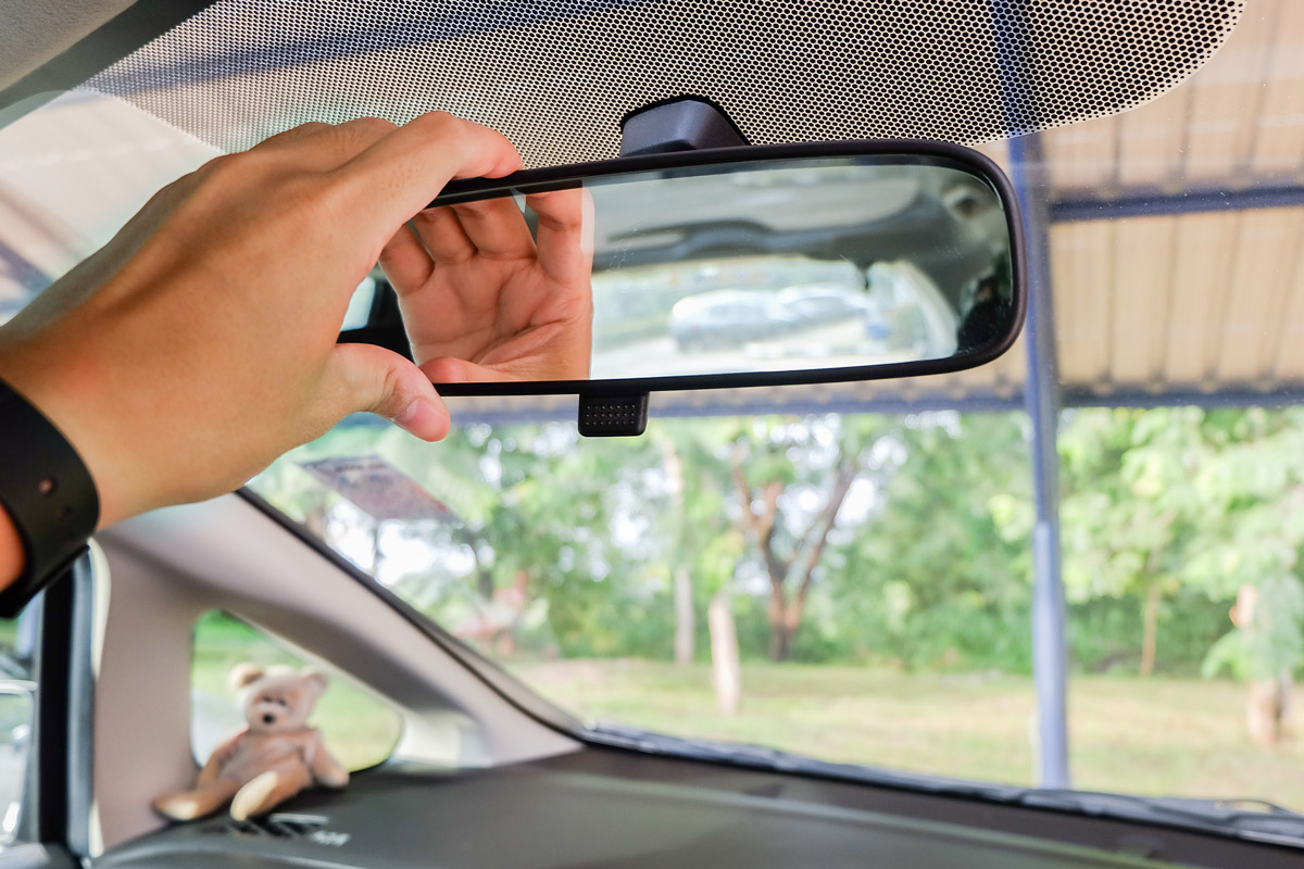 A man adjusts his review mirror of his car to better see out the back window