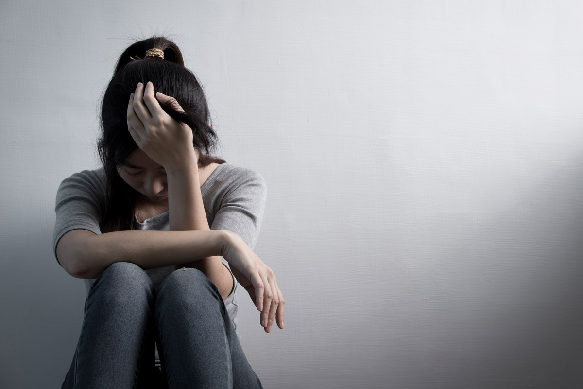 A young girl sitting curled up against a wall with her head in her hands