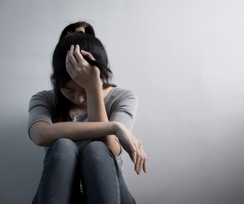 A young girl sitting curled up against a wall with her head in her hands