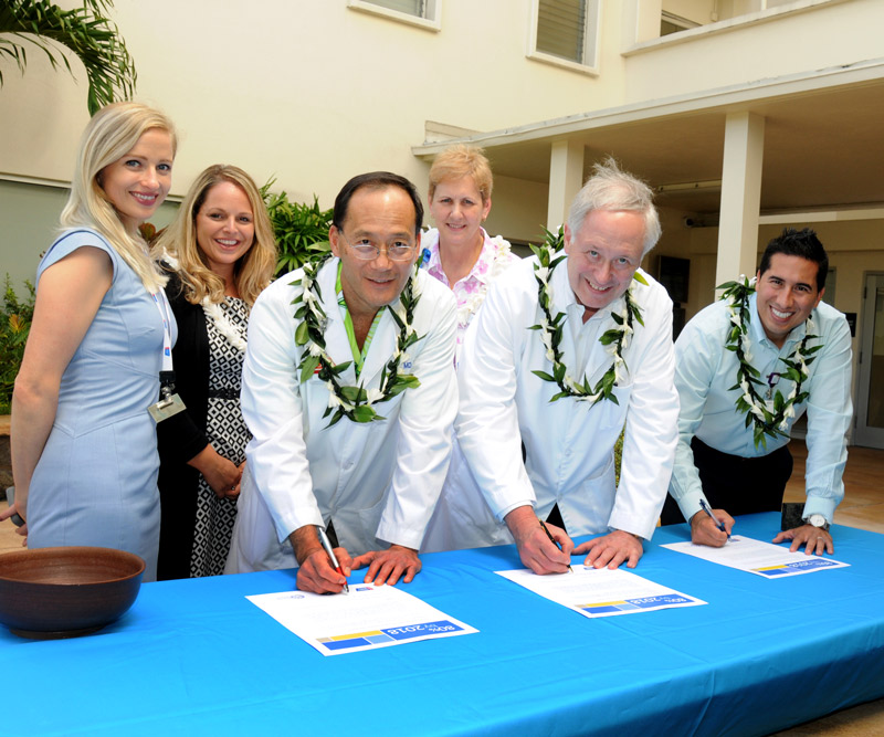 A group of people stand around a table signing a commitment pledge to show their support of a program.