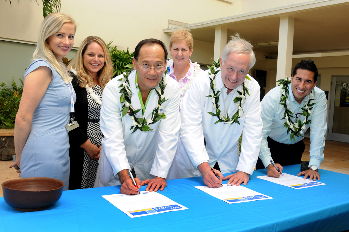 A group of people stand around a table signing a commitment pledge to show their support of a program.