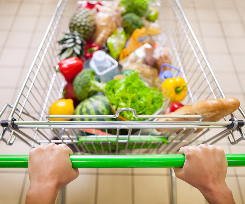 A man pushes a grocery cart full of fresh fruits and vegetables