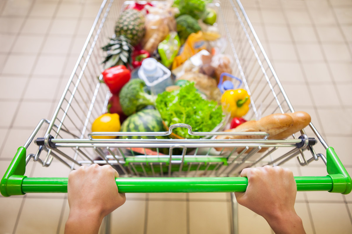 A man pushes a grocery cart full of fresh fruits and vegetables