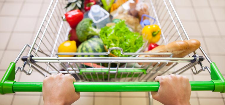 A man pushes a grocery cart full of fresh fruits and vegetables