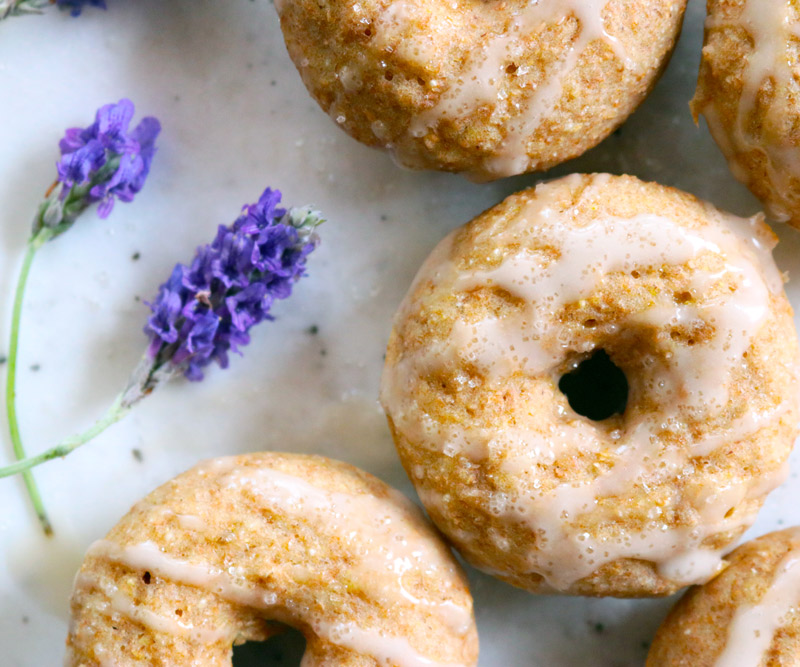 A batch of Baked Lavender & Rose Donuts are displayed on a counter top with fresh sprigs of lavender next to them